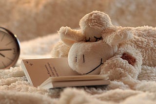 A cute image of a lamb plushie with closed eyes and an alarm clock.