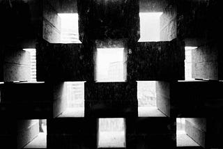 Concrete wall with a grid of square openings casting geometric shadows and light patterns from outside.