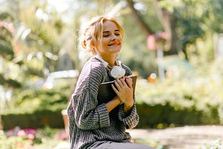 Close-up portrait of woman sitting in greenhouse with headphones and book