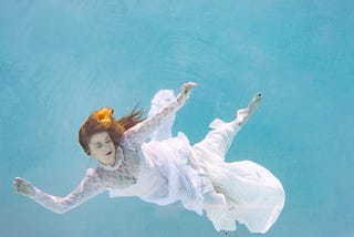 A woman with her eyes closed in a white wedding dress sinking through water