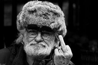 Old man with raccoon hat on giving you the finger, because he doesn’t care what you think.