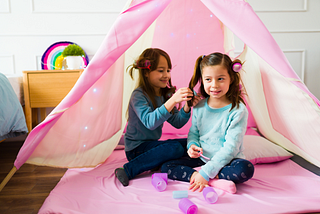 Two girls on a playdate putting curlers in each other’s hair