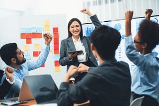 an Asian business woman stands in front of her team as they cheer for her great leadership