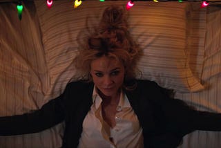 bird’s-eye-view of Cassie in a shirt and jacket, lying on a bed and looking up