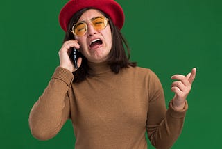 Young woman crying while on the phone, wearing a red hat. The background is green.