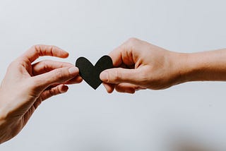 Two hands holding a love shaped card.