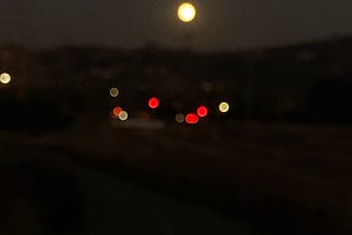 traffic lights in the distance against a backdrop of the bright full moon over the dark hills