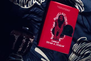 A picture of Monday’s not coming by Tiffany Jackson and a slice of chocolate cake on a mismatche bed spread.