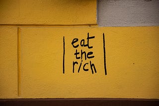 “eat the rich” written on a yellow wall