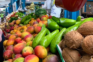 Fruit stand with mangoes, avocados, coconuts and hanging red scale. An Afternoon in La Plaza. Kim Vazquez author.