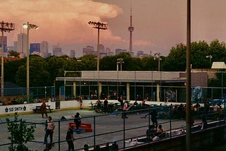A group of skaters skating around Christie Pits Skate Park at sunset.