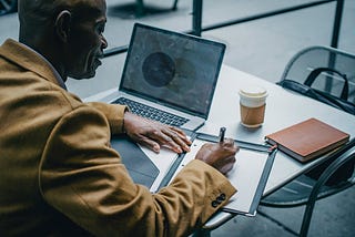 https://www.pexels.com/photo/crop-black-businessman-writing-on-paper-near-laptop-in-cafeteria-5648032/