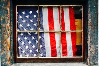 American flag behind a window in a distressed house.