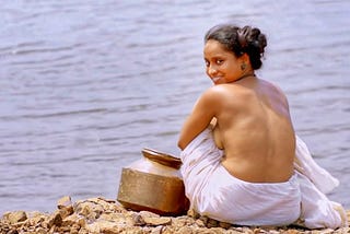 A semi- nude lady sitting on the banks of a river