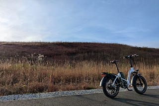 A white e-bike in the foreground, against an autumn field and blue sky in the background.
