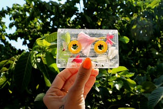 Hand with orange nail polish holds clear cassette Mixtape with flower petals inside it.
