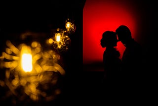 A silhoutte photo of a couple with red lit background as their foreheads are pressed against one another.