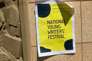 A paper sign advertising “National Young Writers’ Festival” blu-tacked on a sandstone building