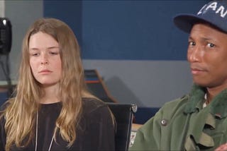Maggie Rogers looks solemnly at the floor, while to our right, Pharrell Williams looks surprised towards the camera.