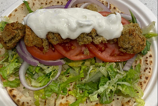 Three yellow pea falafels in a warm whole grain pita with hummus, lettuce, tomato, and onion, topped with tzatziki sauce.