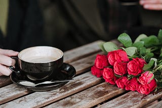 Faceless couple with coffee and rose bouquet in cafeteria