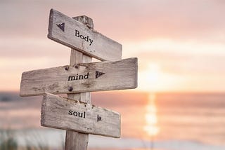 Body, Mind and Soul text quote engraved on wooden signpost outdoors on the beach with sunset theme. By Jon Anders Wiken