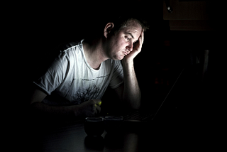 A young man in a T-shirt with his hand on his head, looking down and depressed.