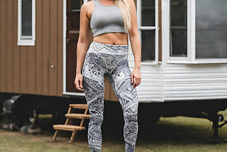 A woman, dressed in a crop top and leggings, stands outside a mobile home.