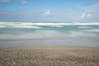Photograph of a beach, ocean and sky in which the waves have been blurred by a long exposure.