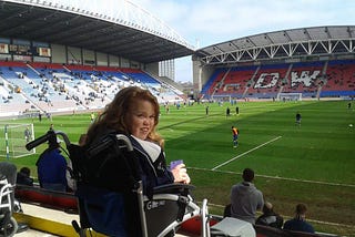 Alex in wheelchair smiling in front of pitch