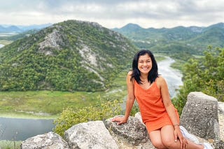 Lady in an orange dress with a lake and green hill in the background