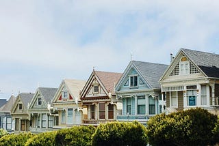 A row of houses in various colors with bushes in front.