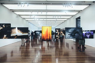 An open, well-lit, white room with a series of colorful images in frames suspended from the ceiling.