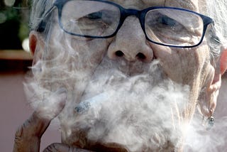 Close-up of old woman exhaling cigarette smoke.