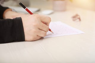 A hand holding a pencil fills out a scantron bubble sheet.