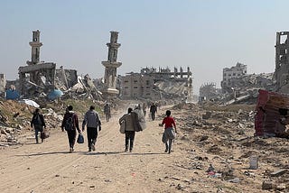 Several individuals walk with backs to camera through a war-torn area