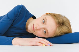 A woman with a somber expression, lying on her side on a white surface