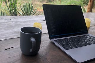 A MacBook pro with a cup of coffee sits on a wooden desk