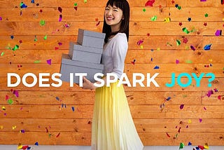 Marie Kondo smiling at the camera while carrying boxes. Caption reads: Does it spark joy?