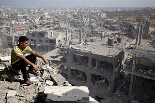 A boy sits atop the rubble of a destroyed Gaza building — against a landscape of ruins — after Israeli saturation bombing of his homeland in occupied Palestine.