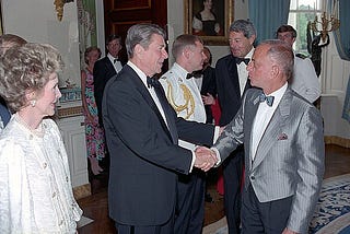 President Reagan shaking Roy Cohn’s hand, Nancy Reagan looking on, at a fancy dress event in the White House.
