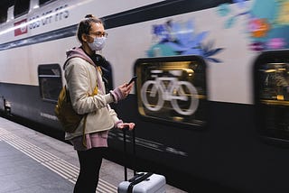 A girl with face mask standing in front of a moving train