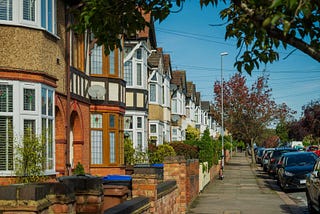 Residential street in West London with terraced houses, parked cars and tree-lined pavement on a clear day
