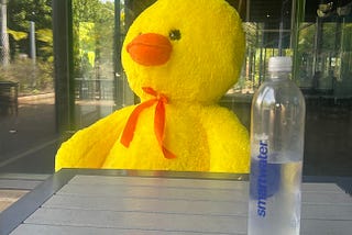 photo of a giant duck plushie sitting by itself at a table staring off into the distance