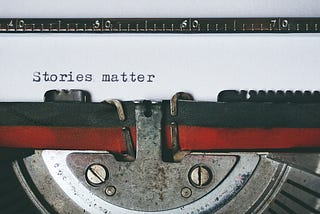 Typewriter close up of black and red ribbon with “Stories matter” typed on white paper