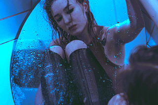A girl looking in a mirror in the bath tub and she is very sad.