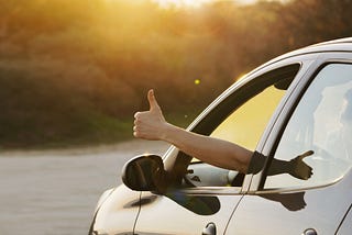 Person sticking thumbs up outside of car window