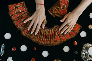 An image of tarot cards fanned out over a table and the reader’s hands hovering over them.