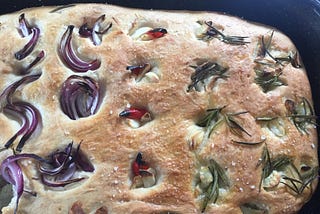 A homebaked focaccia bread loaf with red onions, chilis, rosemary, garlic, and sea salt.