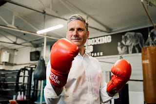 Keir Starmer stands with boxing gloves on is shown smiling at the camera